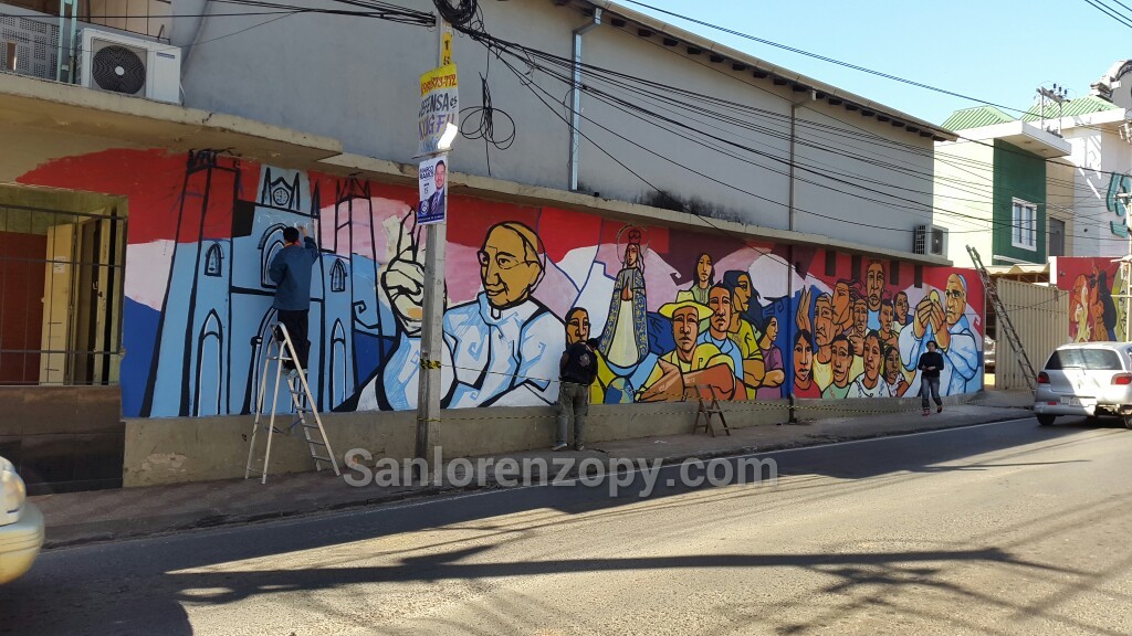 La dibujos de la Catedral, el Papa, la Virgen, grupo de campesinos e indígenas y el momento de la comunión completan la pintura realizada por uno de los muros de la casa parroquial.